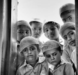 A group of children in traditional attire gazing through a window with solemn expressions.