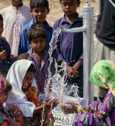 Group of children collecting clean water from a pump in an outdoor setting.
